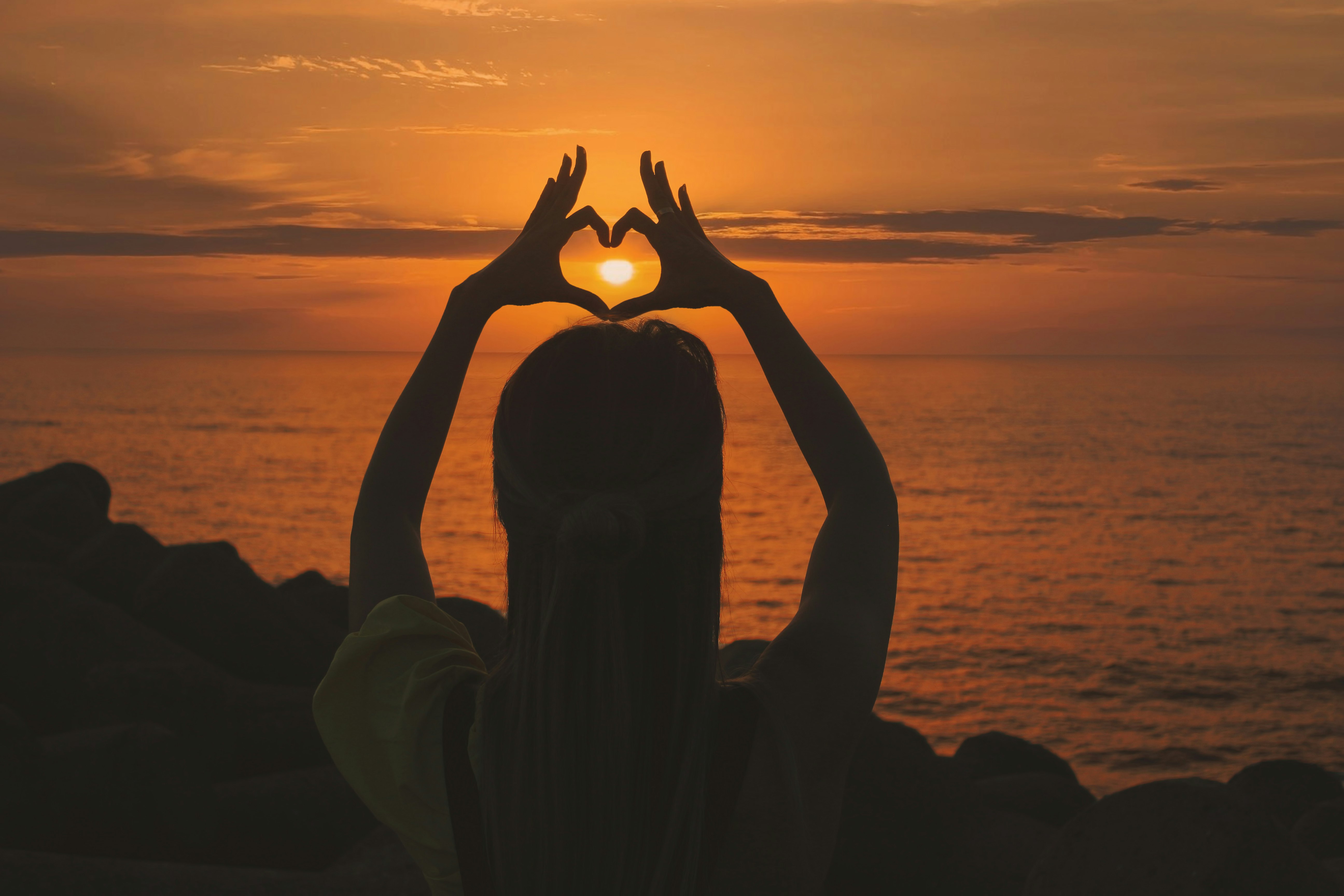 silhouette of woman doing heart sign during sunset